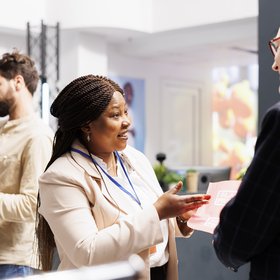 Une femme tient un flyer dans sa main. Elle discute avec un homme.