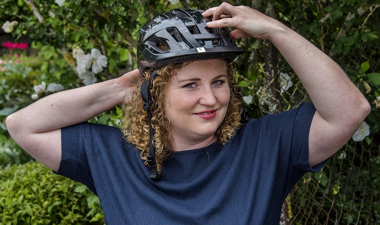 Eine junge Frau mit bloden Locken zieht einen Helm an.