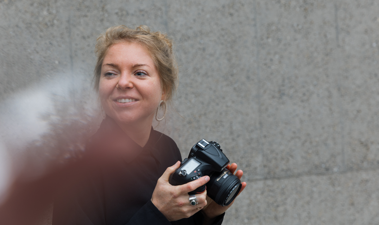 Damaris B. Künstlerisches Foto von Damaris B. Sie lächelt mit dem Blick nach links und mit der Fotokamera in der Hand.